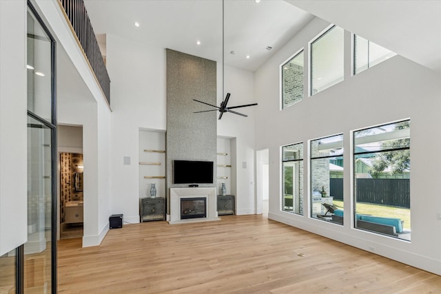 unfurnished living room featuring light wood-type flooring, a ceiling fan, a wealth of natural light, and a glass covered fireplace