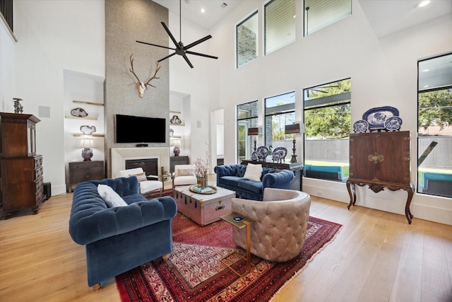 living room featuring built in shelves, light wood-style flooring, a fireplace, and a ceiling fan