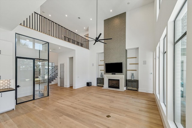 unfurnished living room with built in shelves, a fireplace, a ceiling fan, stairs, and light wood finished floors