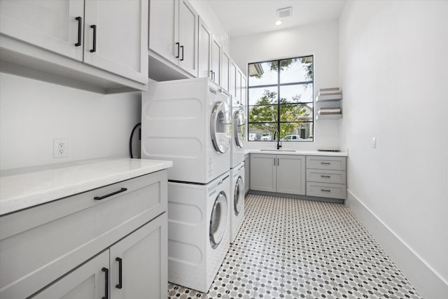 laundry area with a sink, visible vents, stacked washer / drying machine, cabinet space, and light floors