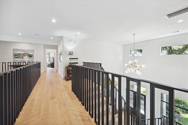 corridor featuring visible vents, light wood-style flooring, an upstairs landing, a notable chandelier, and recessed lighting