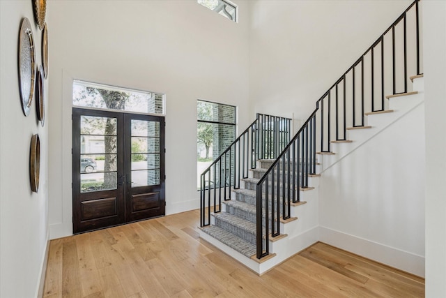 entrance foyer with french doors, stairway, light wood-style flooring, a towering ceiling, and baseboards