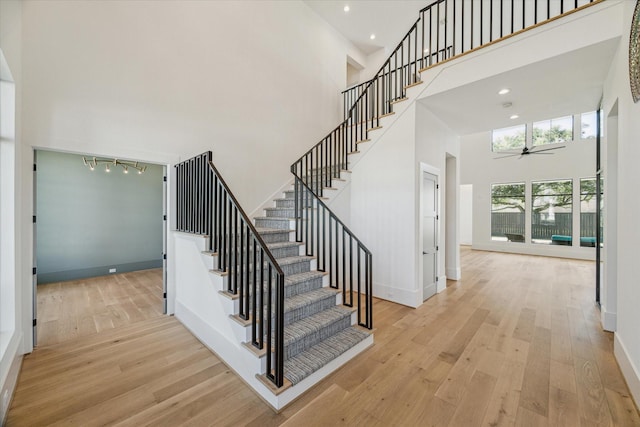 stairway with a towering ceiling, ceiling fan, baseboards, and hardwood / wood-style floors