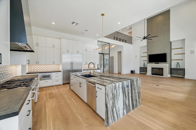 kitchen with visible vents, high end appliances, wall chimney exhaust hood, light wood-style floors, and a sink