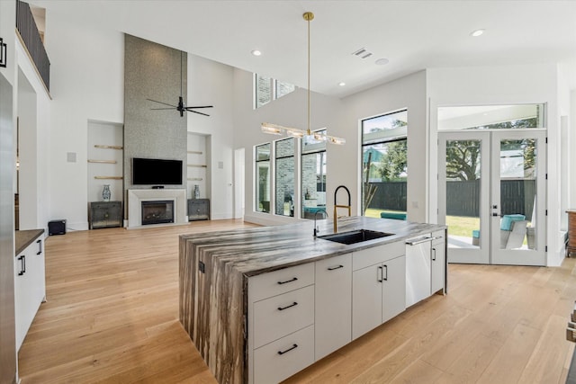 kitchen with light wood finished floors, an island with sink, a fireplace, and a sink