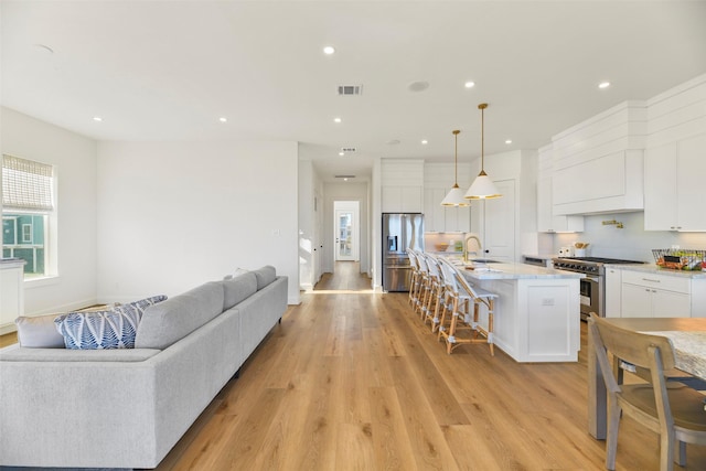 kitchen with a breakfast bar area, visible vents, appliances with stainless steel finishes, light wood-style floors, and open floor plan