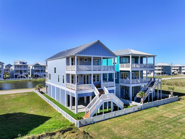 rear view of property featuring a balcony, a water view, stairs, fence, and a yard