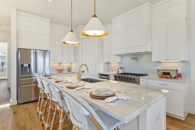 kitchen featuring stainless steel appliances, a sink, white cabinets, light wood-type flooring, and tasteful backsplash