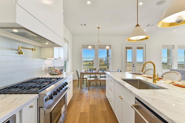 kitchen with custom exhaust hood, stainless steel appliances, light wood-style floors, white cabinets, and a sink