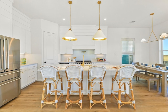 kitchen with light wood-style flooring, white cabinetry, hanging light fixtures, backsplash, and freestanding refrigerator