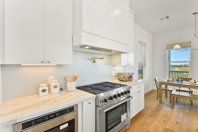 kitchen with high end stainless steel range, decorative backsplash, visible vents, and white cabinets