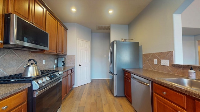 kitchen with visible vents, light wood-style flooring, appliances with stainless steel finishes, dark countertops, and backsplash