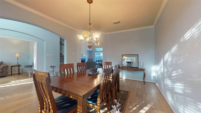 dining space featuring light wood finished floors, arched walkways, crown molding, and an inviting chandelier