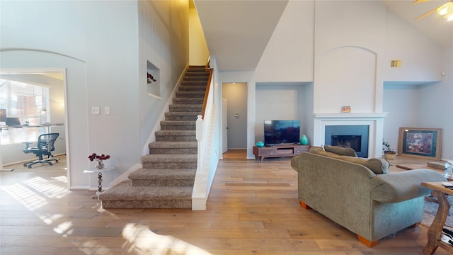 living room with high vaulted ceiling, light wood-style flooring, stairway, a fireplace, and baseboards