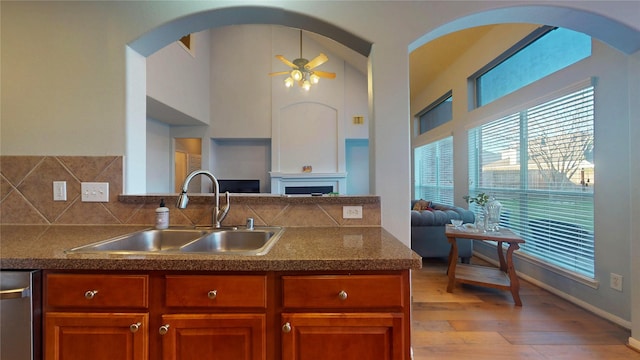 kitchen featuring brown cabinets, a ceiling fan, a sink, stainless steel dishwasher, and open floor plan