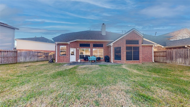 rear view of property featuring brick siding, a fenced backyard, a patio, and a yard