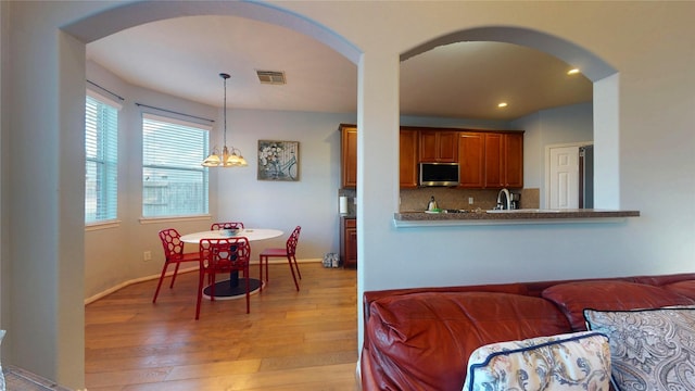 kitchen with stainless steel microwave, arched walkways, visible vents, and light wood finished floors