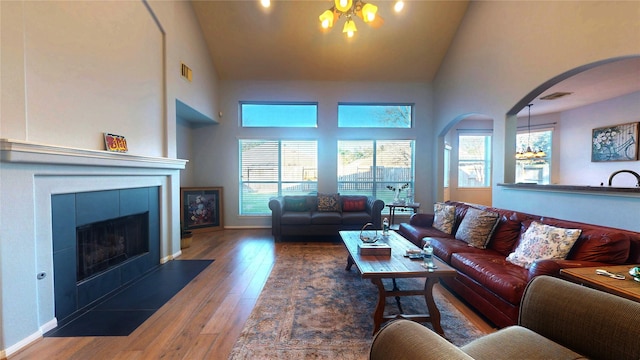 living area with a wealth of natural light, wood finished floors, arched walkways, and a chandelier