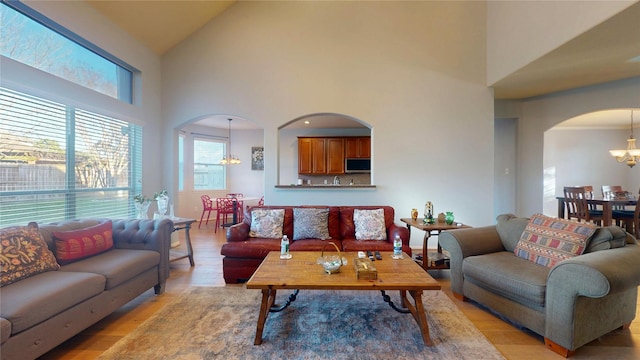 living area with arched walkways, a notable chandelier, light wood-style flooring, and lofted ceiling