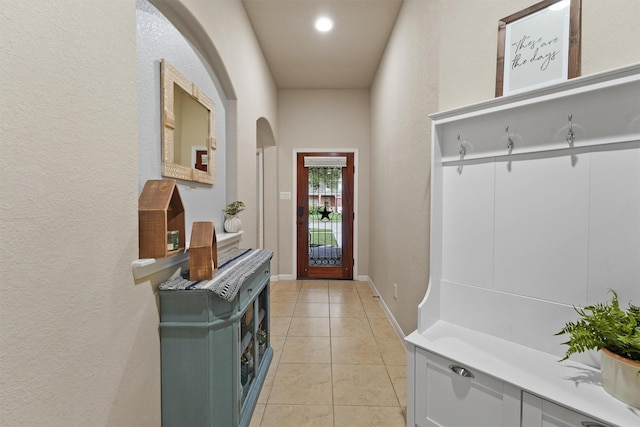 mudroom featuring light tile patterned floors, arched walkways, and baseboards