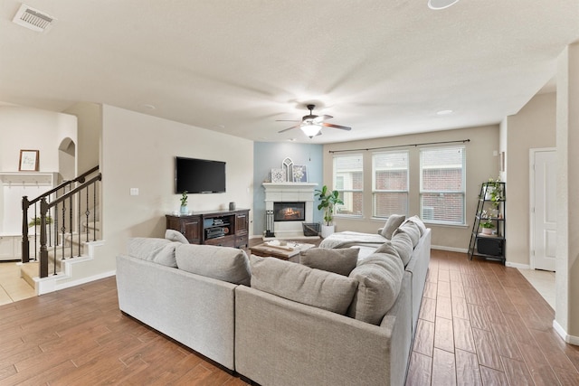 living area featuring visible vents, stairway, wood finished floors, and a glass covered fireplace