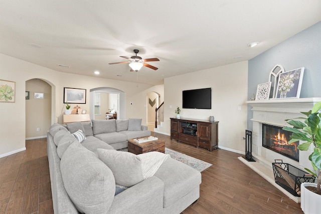 living room featuring baseboards, arched walkways, dark wood finished floors, and a glass covered fireplace