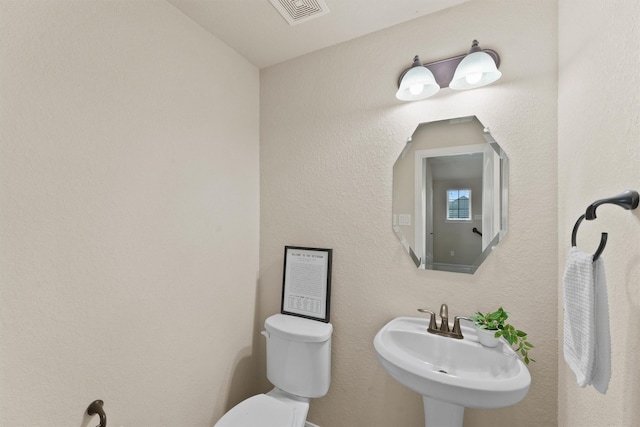 half bath with visible vents, a sink, and toilet