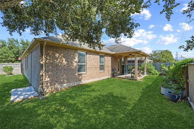 rear view of house with a ceiling fan, a patio, a fenced backyard, a yard, and brick siding