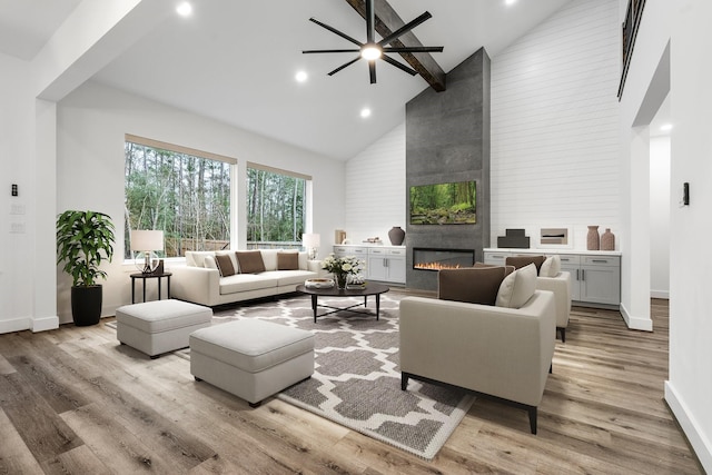 living area with high vaulted ceiling, light wood-style flooring, a large fireplace, baseboards, and beamed ceiling