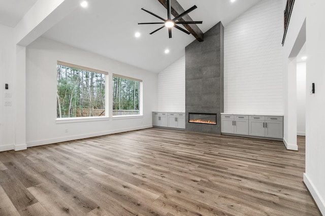 unfurnished living room featuring high vaulted ceiling, a fireplace, wood finished floors, baseboards, and beam ceiling