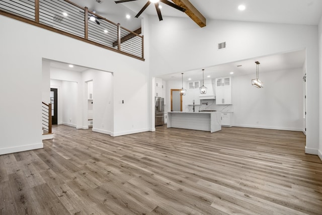 unfurnished living room featuring light wood-type flooring, stairs, baseboards, and beamed ceiling