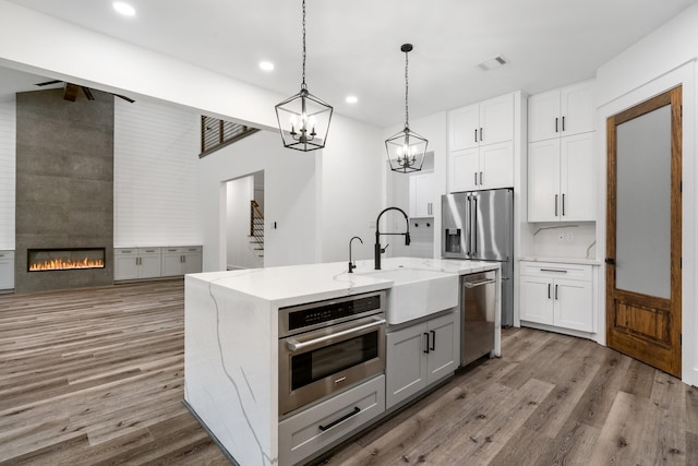 kitchen with light stone counters, a large fireplace, stainless steel appliances, wood finished floors, and a sink