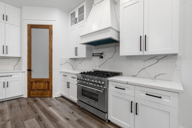 kitchen featuring custom exhaust hood, glass insert cabinets, white cabinetry, wood finished floors, and high end stove