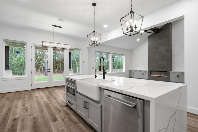 kitchen with light stone counters, light wood-style flooring, a large fireplace, visible vents, and stainless steel dishwasher