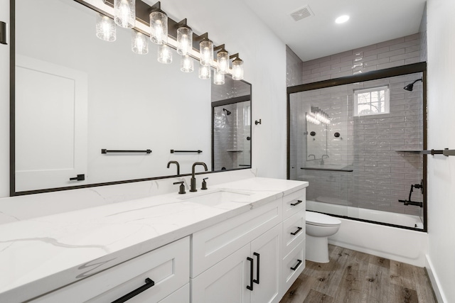 bathroom with visible vents, toilet, enclosed tub / shower combo, wood finished floors, and vanity