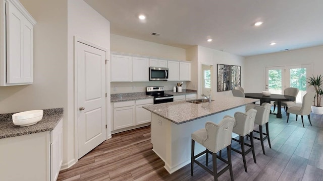 kitchen featuring wood finished floors, appliances with stainless steel finishes, a sink, and white cabinets