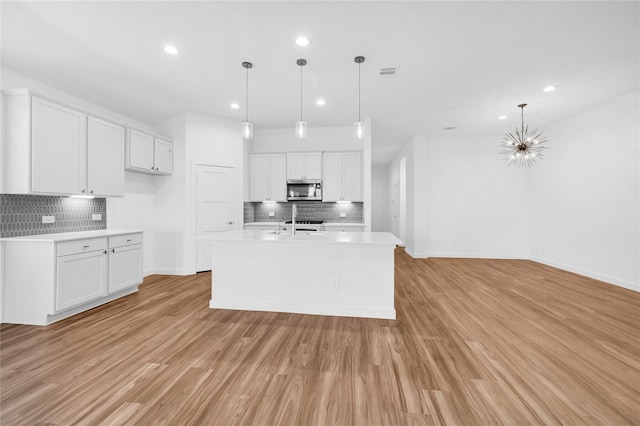 kitchen with light countertops, light wood finished floors, stainless steel microwave, and white cabinetry