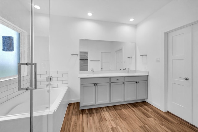 full bath with a bath, double vanity, a sink, and wood finished floors