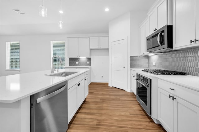 kitchen featuring stainless steel appliances, a sink, visible vents, light wood finished floors, and pendant lighting