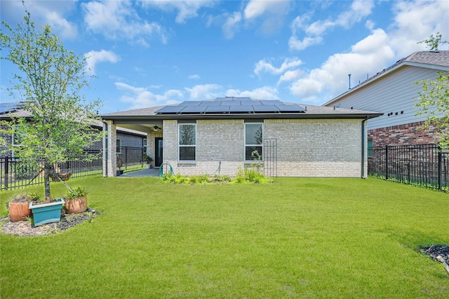 back of house featuring a yard, brick siding, a fenced backyard, and roof mounted solar panels