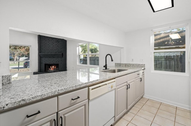 kitchen featuring light tile patterned floors, white dishwasher, a fireplace, a sink, and light stone countertops