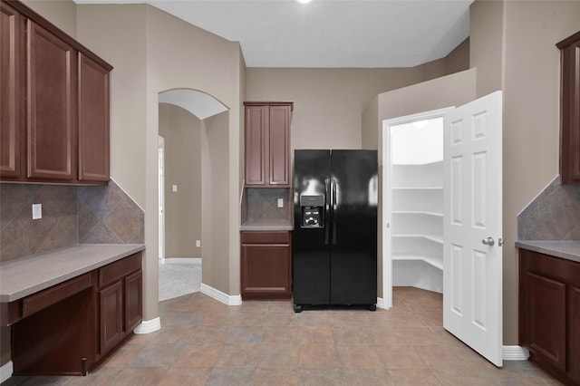 kitchen featuring decorative backsplash, arched walkways, black fridge with ice dispenser, and light countertops