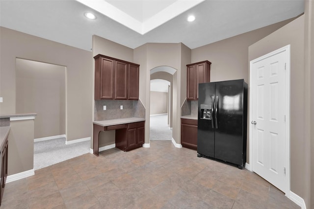 kitchen with tasteful backsplash, arched walkways, light countertops, baseboards, and black refrigerator with ice dispenser