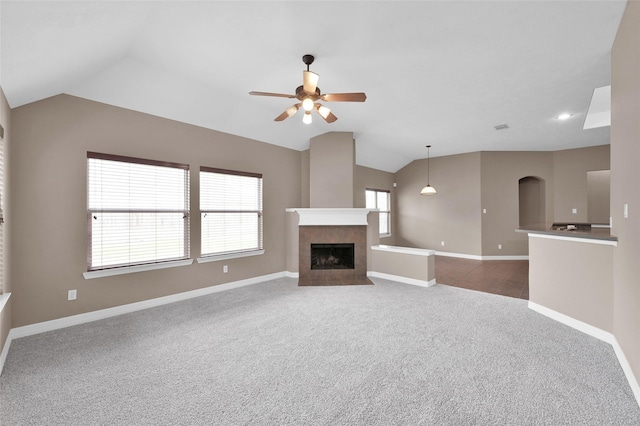 unfurnished living room featuring a ceiling fan, baseboards, a tile fireplace, vaulted ceiling, and carpet flooring