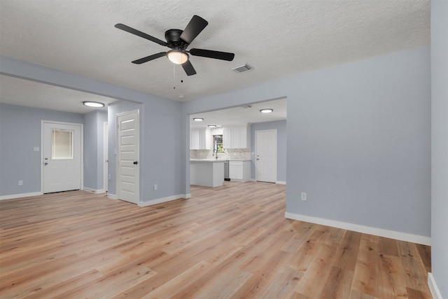 unfurnished living room with a textured ceiling, a ceiling fan, visible vents, baseboards, and light wood finished floors