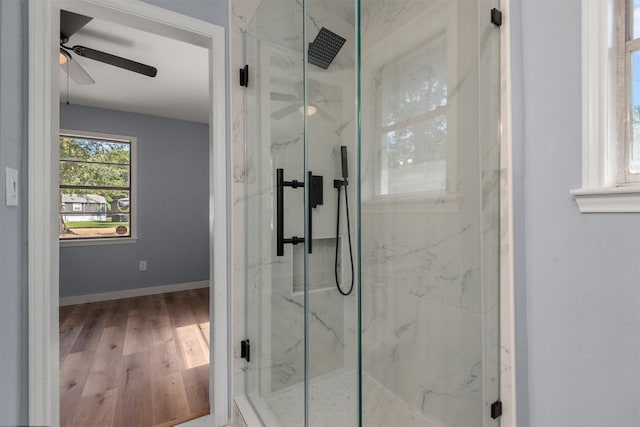 full bath with wood finished floors, a marble finish shower, a ceiling fan, and baseboards