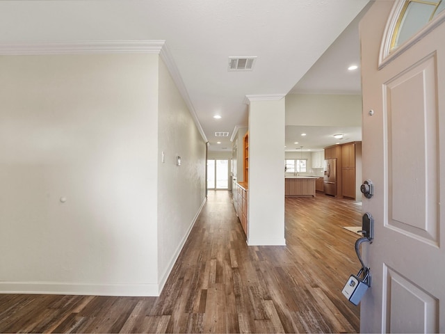 corridor featuring baseboards, visible vents, wood finished floors, and ornamental molding