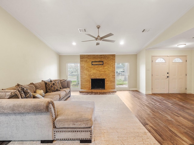 living room with baseboards, visible vents, wood finished floors, crown molding, and a fireplace