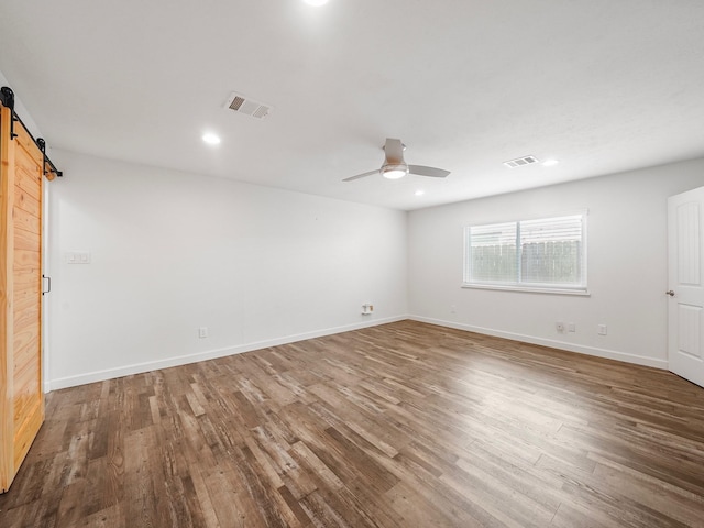 empty room featuring a ceiling fan, a barn door, visible vents, and wood finished floors