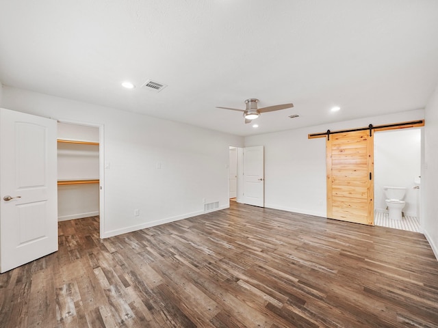 unfurnished bedroom with recessed lighting, wood finished floors, visible vents, and a barn door